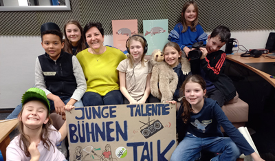 Foto der Kinderreporter*innen mit selbstgebastelten Plakat "Junge Talente - Bühnen Talk"